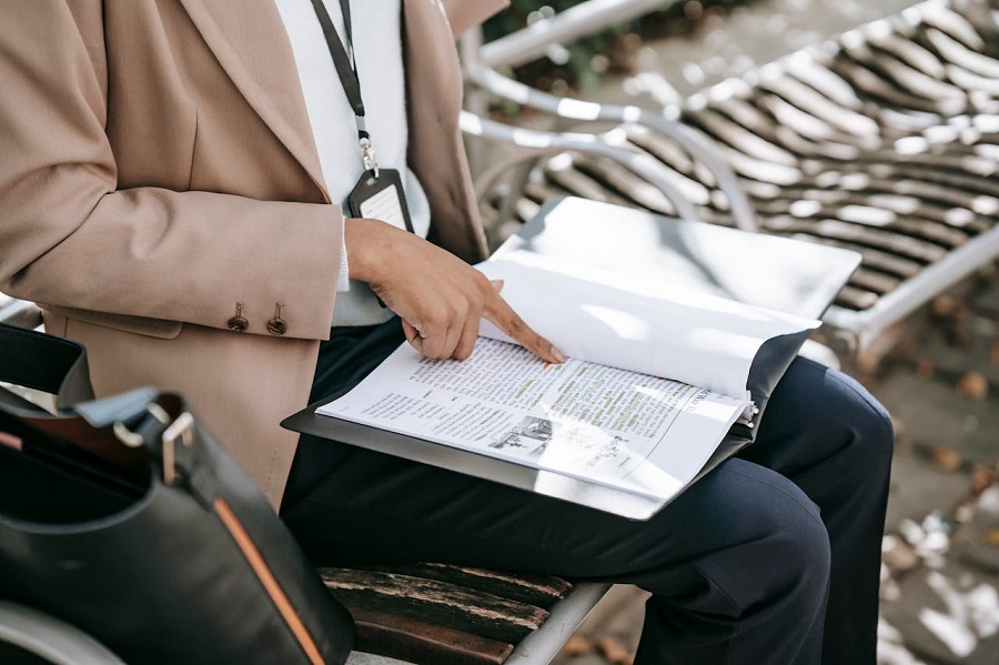 personne-en-blazer-marron-et-pantalon-noir-assis-sur-une-chaise-en-lisant-un-livre